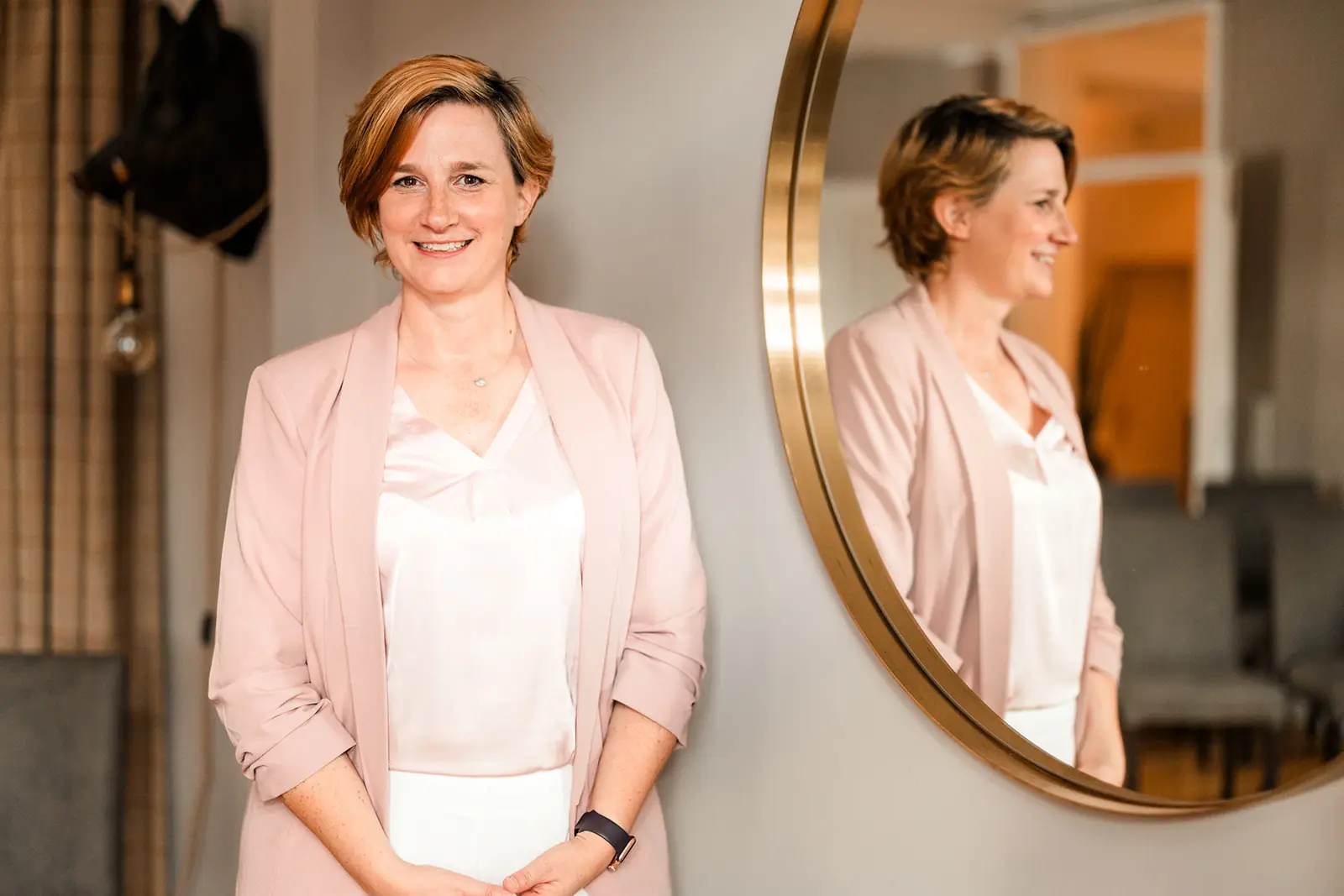 Hochzeitsplanerin Caro Kühle-Lange von federleicht HOCHZEITEN in rosafarbenem Blazer neben einem runden Spiegel.